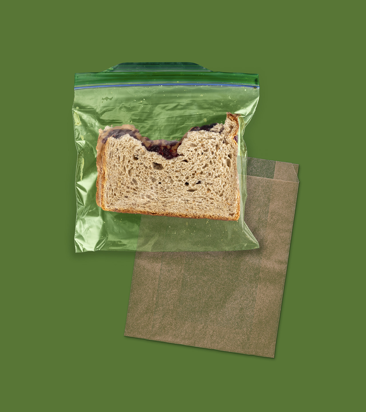 Half eaten sandwich in a plastic bag and a wax paper bag in the background.